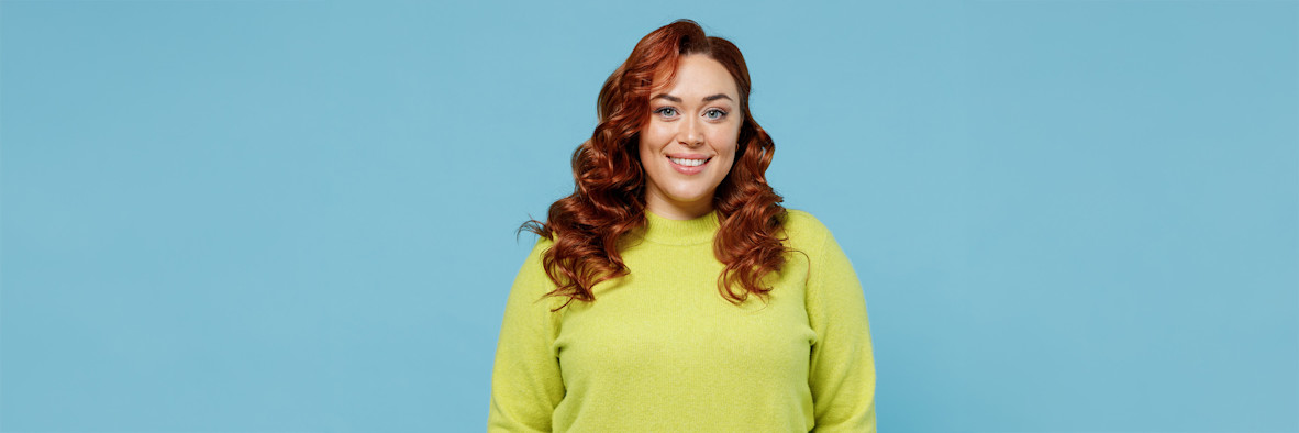 A cheerful red-haired woman in a yellow-green top smiling against a matching background.