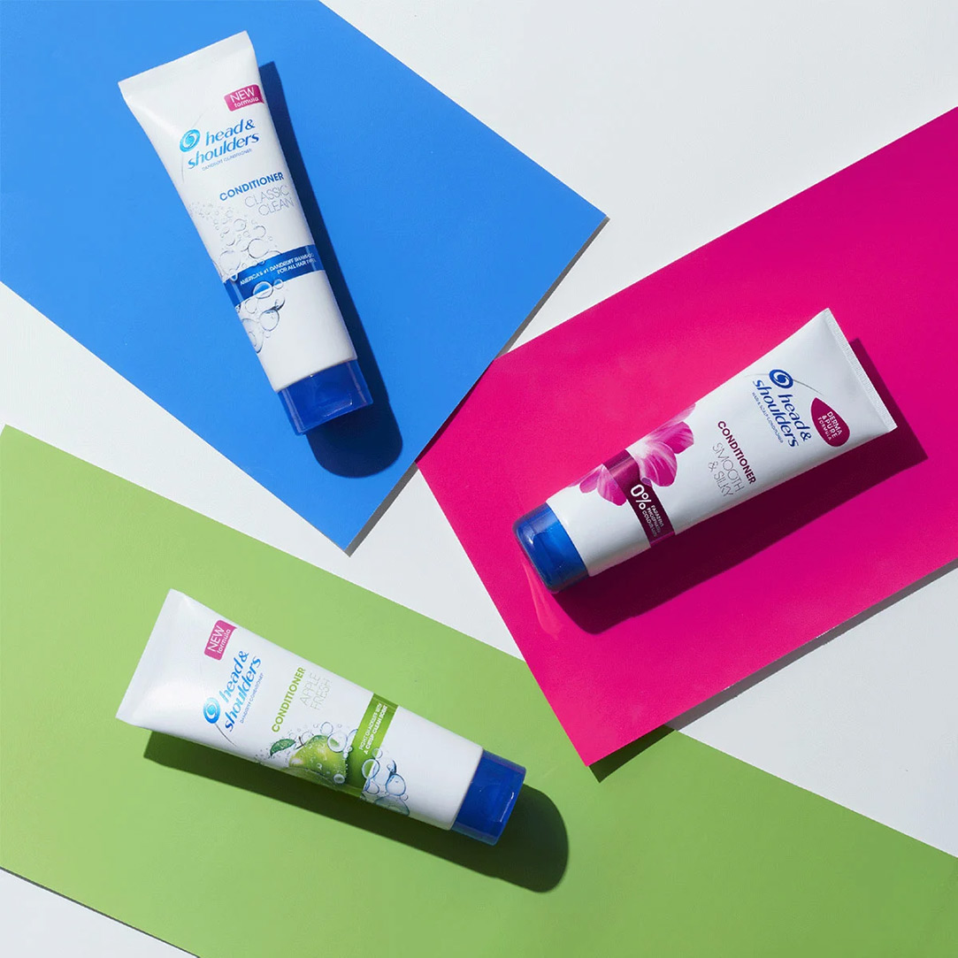 Head & Shoulders conditioner bottles lying on three different pieces of paper: blue, green and pink. 