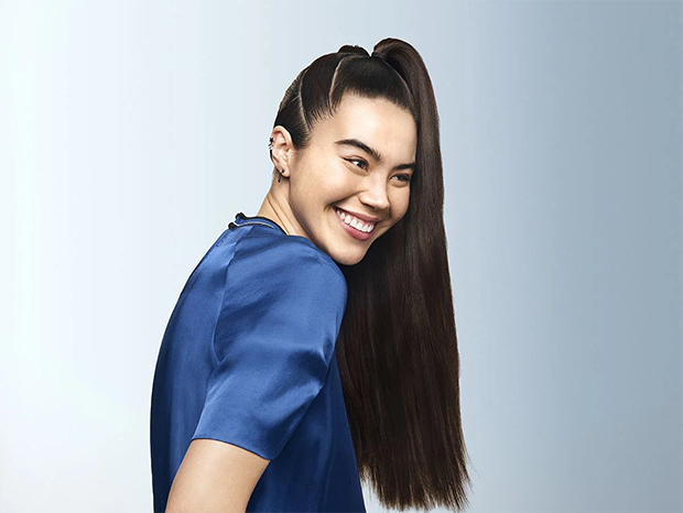 A woman with very long, dark and shiny hair with styled ponytail, laughing.