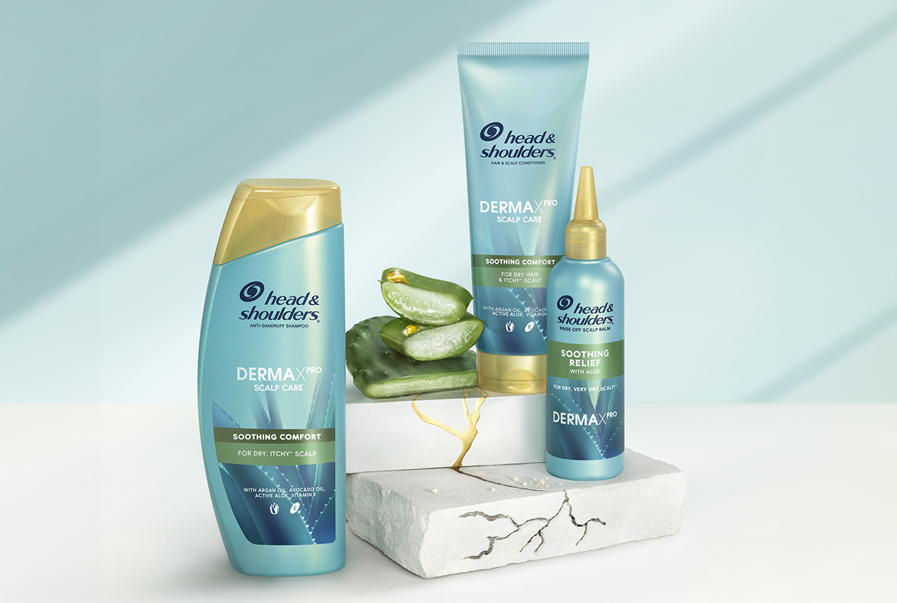 Derma X Pro Soothing comfort Head & Shoulders shampoo, conditioner and scalp balm bottles, next to aloe and cactus pieces