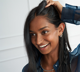 Young woman with long dark hair is smiling and touching her hair.