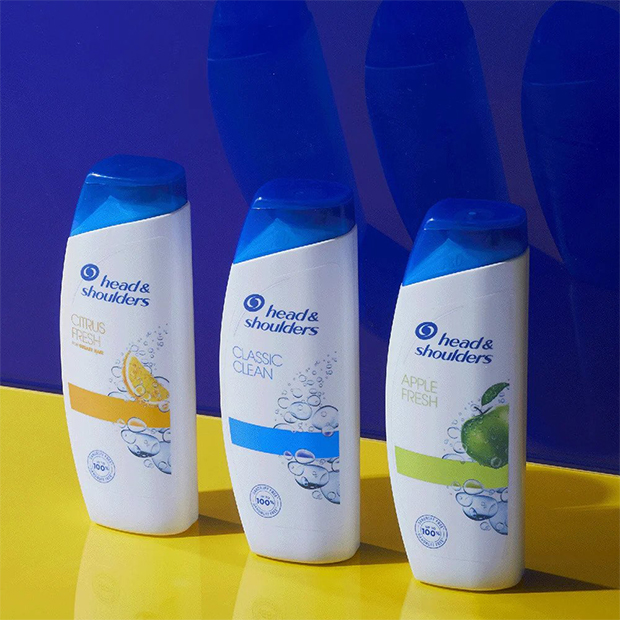 Bottles of Citrus Fresh Shampoo, Classic Clean Shampoo and Apple Fresh Shampoo on a yellow table, on a navy blue background