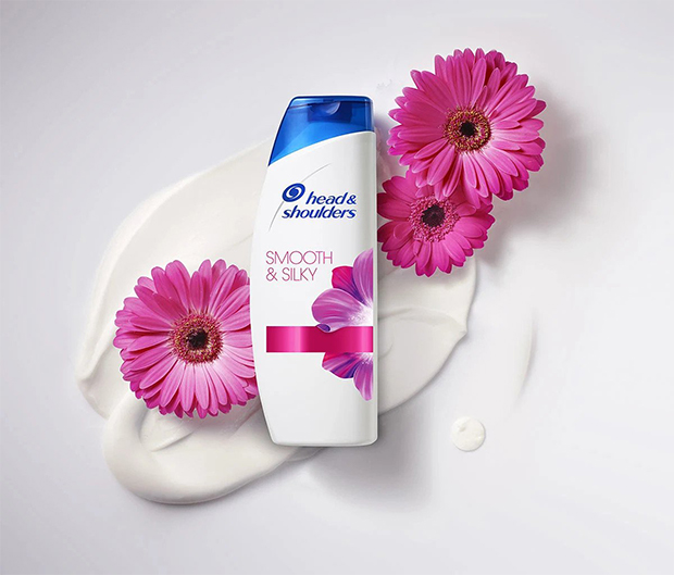 Head&Shoulders Smooth&Silky shampoo bottle lying in the creamy blot with pink gerberas on the sides. 