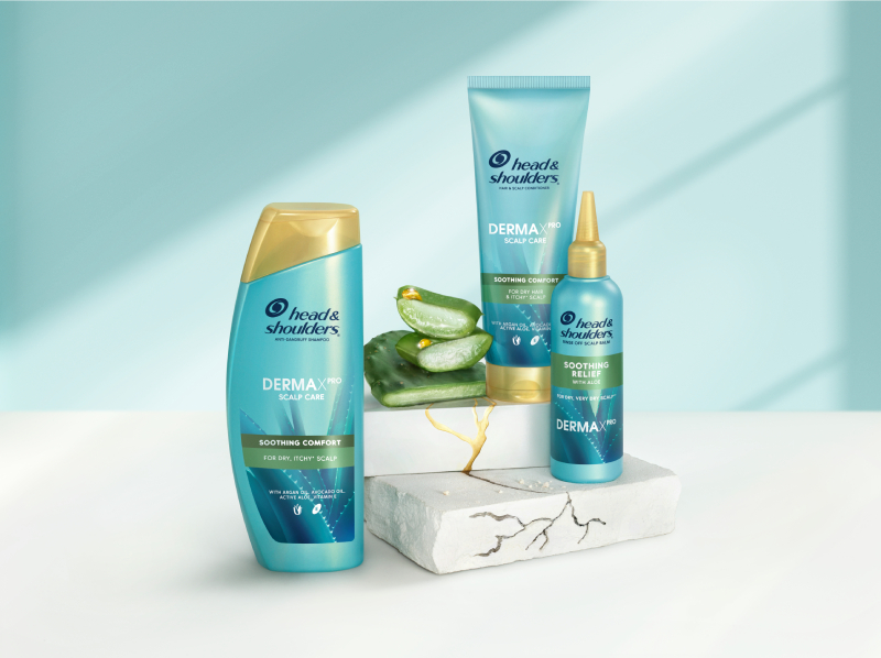 Derma X Pro Soothing comfort Head & Shoulders shampoo, conditioner and scalp balm bottles, next to aloe and cactus pieces
