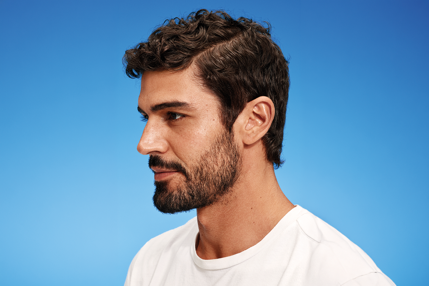 A man with thick, short, dark hair, positioned in profile to the camera against a blue background.