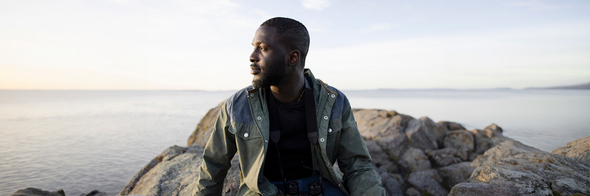 A confident man with natural hair is photographed outdoors in casual clothing.