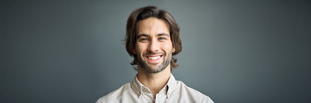 A smiling man with long, healthy-looking dark hair wearing a white shirt.