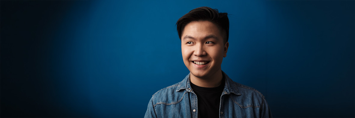 A smiling young Asian man with healthy dark hair against a blue background.