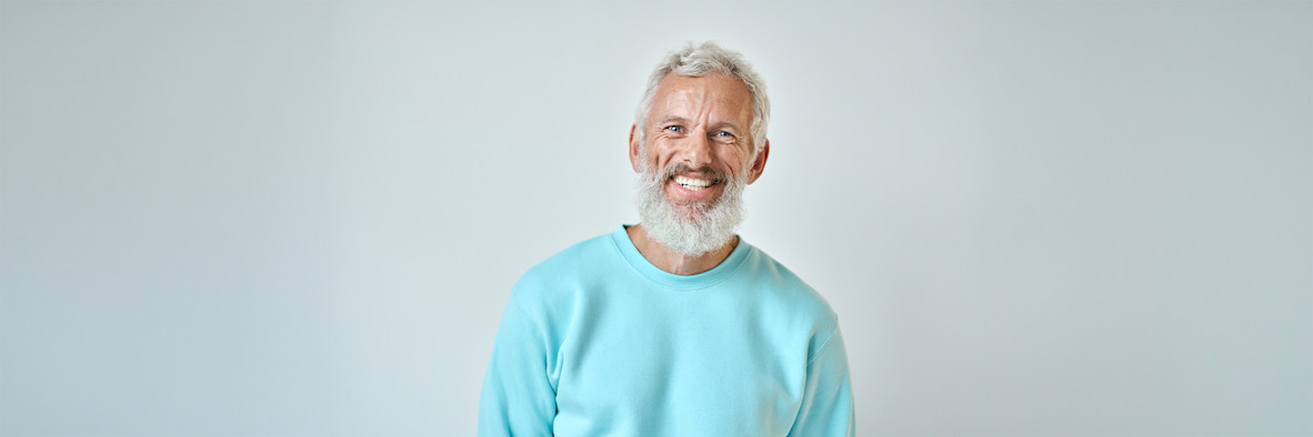 An older man with short grey hair smiles warmly while wearing a teal top.