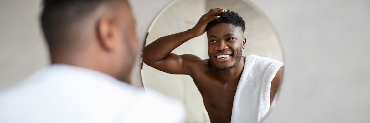 A man touches his scalp with a concerned expression in front of a mirror.