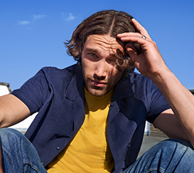 A man with middle-length hair is touching up his hair.