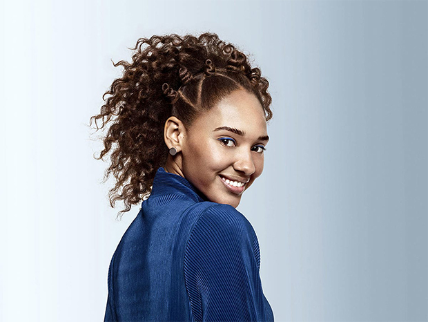 A woman with brown curly hair, looking at the camera and smiling 