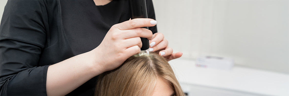 A pair of hands uses scissors to precisely trim dark hair close to the scalp.