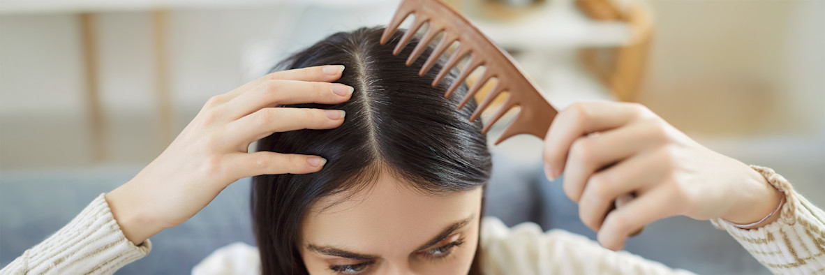 A woman uses a fine-tooth comb to part and comb through her dark hair.