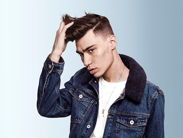 A young man with stylish modern hairstyle holding his hair and looking at the camera.