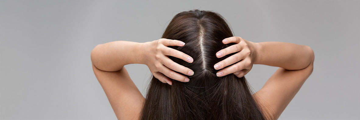 A woman is seen from behind, pulling her long hair over one shoulder to examine it.