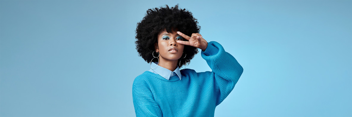 A woman in a blue top points upward while touching her natural curly hair.