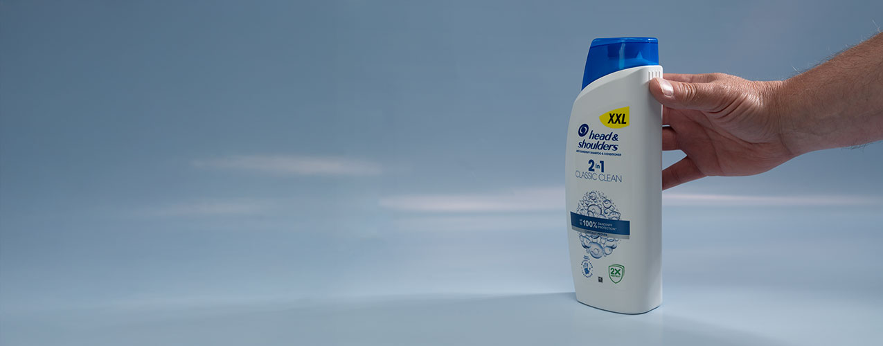 A hand holding a bottle of Head & Shoulders, touching the 4 raised lines on the bottle edge indicating it’s a shampoo.