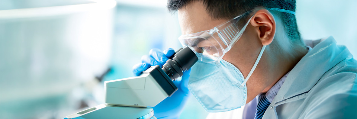 A researcher in a lab coat peers into a microscope, studying samples closely.