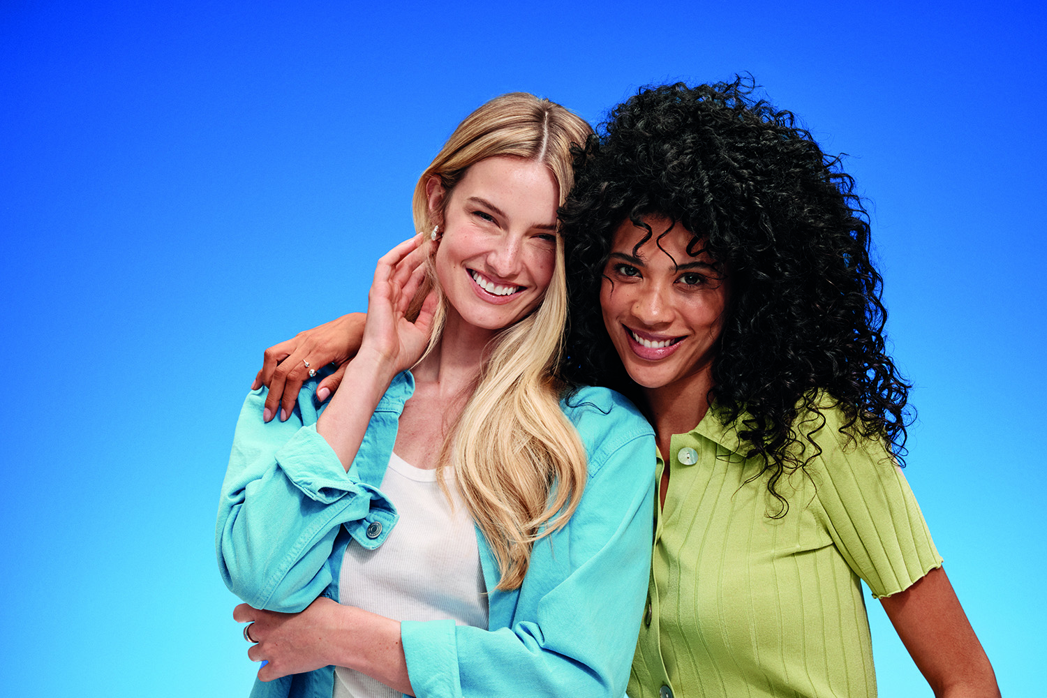 Two smiling women with different hair types pose together.