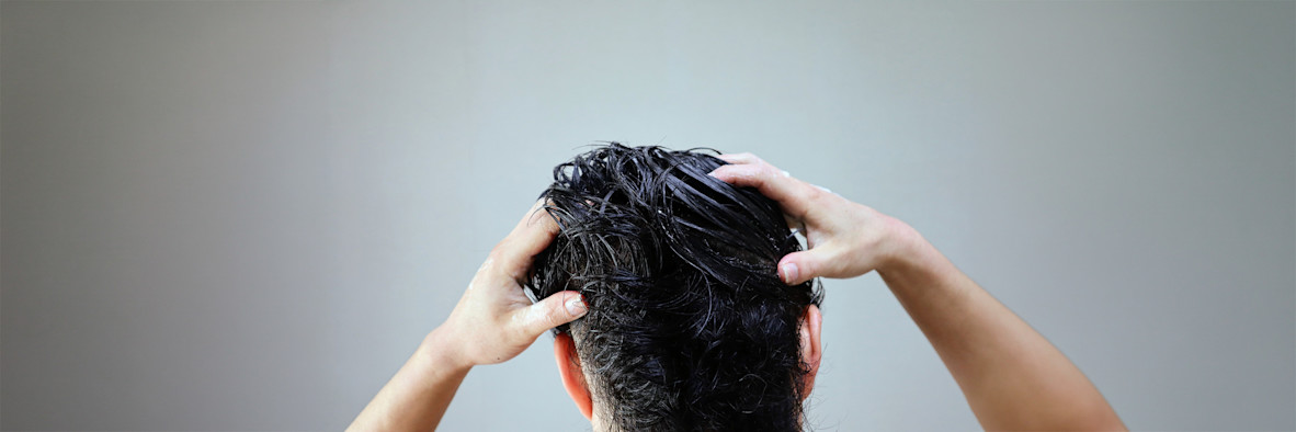 A woman washes her hair with eyes closed, lather visible in her hands.