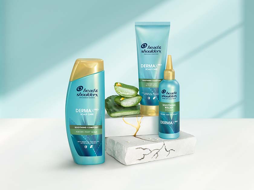 Derma X Pro Soothing comfort Head & Shoulders shampoo, conditioner and scalp balm bottles, next to aloe and cactus pieces