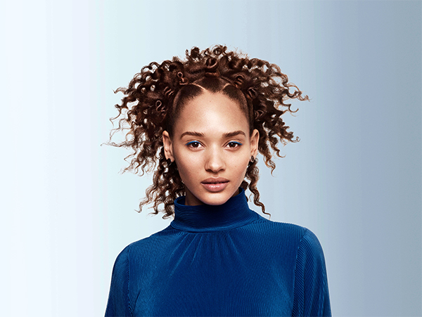 A young woman with curly brown hair pinned up looking at the camera.