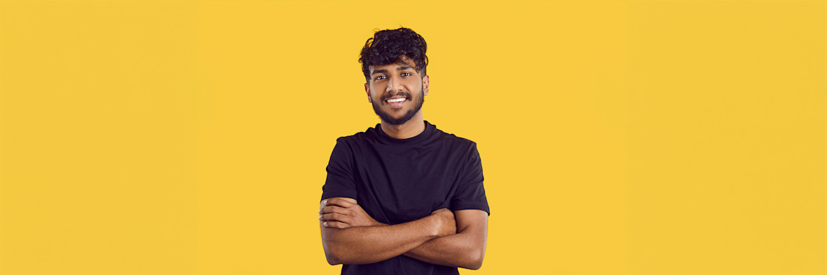 A confident man with dark hair crosses his arms and smiles against a bright yellow background.