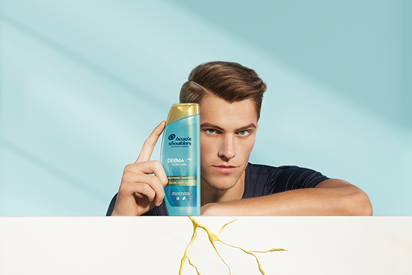 A man resting his arm on the crannied half-wall, holding H&S Derma X Pro Shampoo standing on the same wall by other hand
