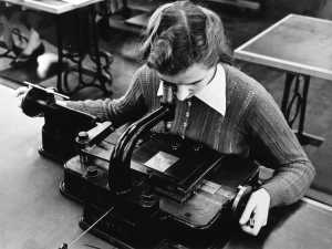 A Monotype employee checking the accuracy of a copper pattern under a microscope. © Monotype archives