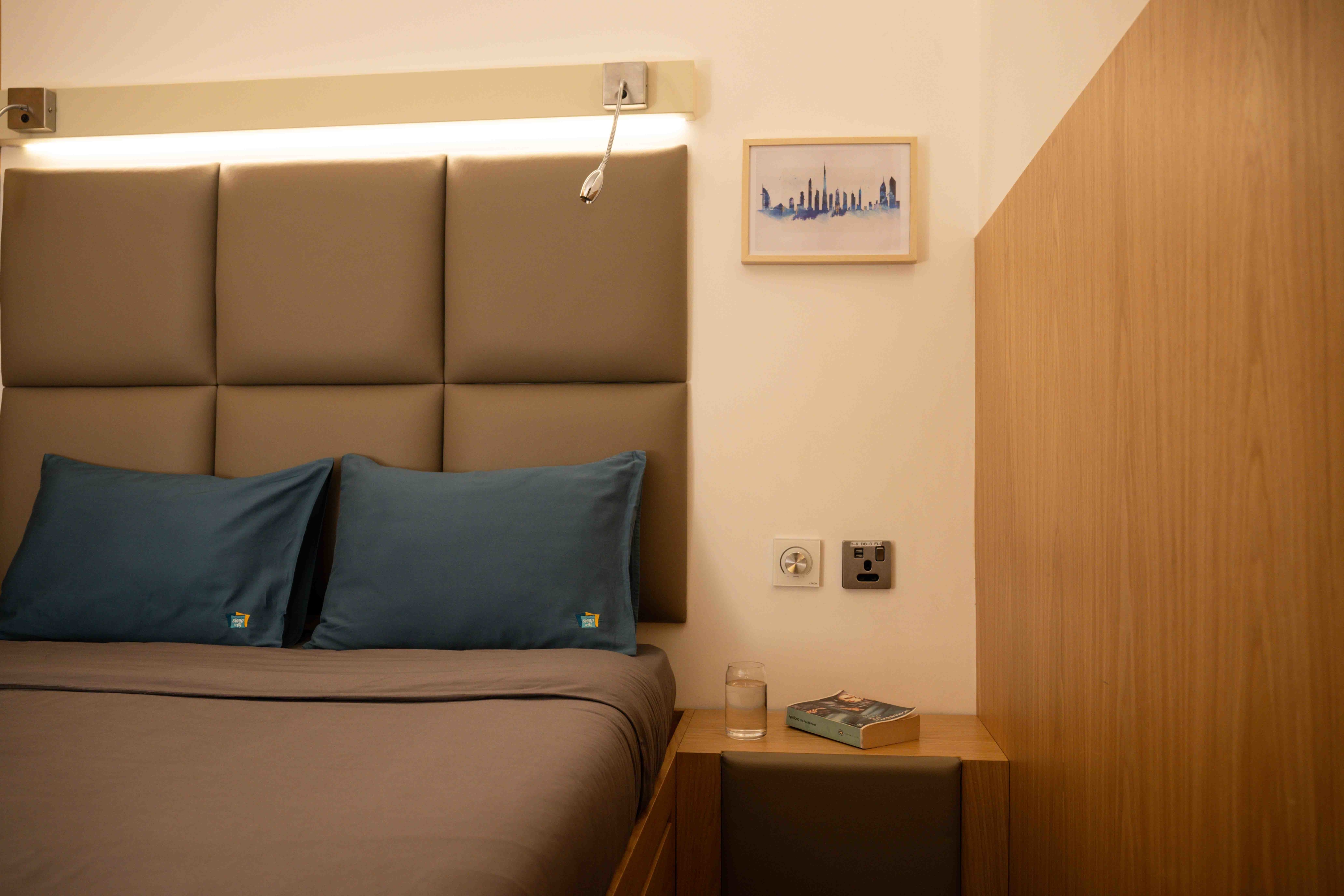 Airport sleep lounge, grey headboard, blue and grey double bed, wooden sidetable 