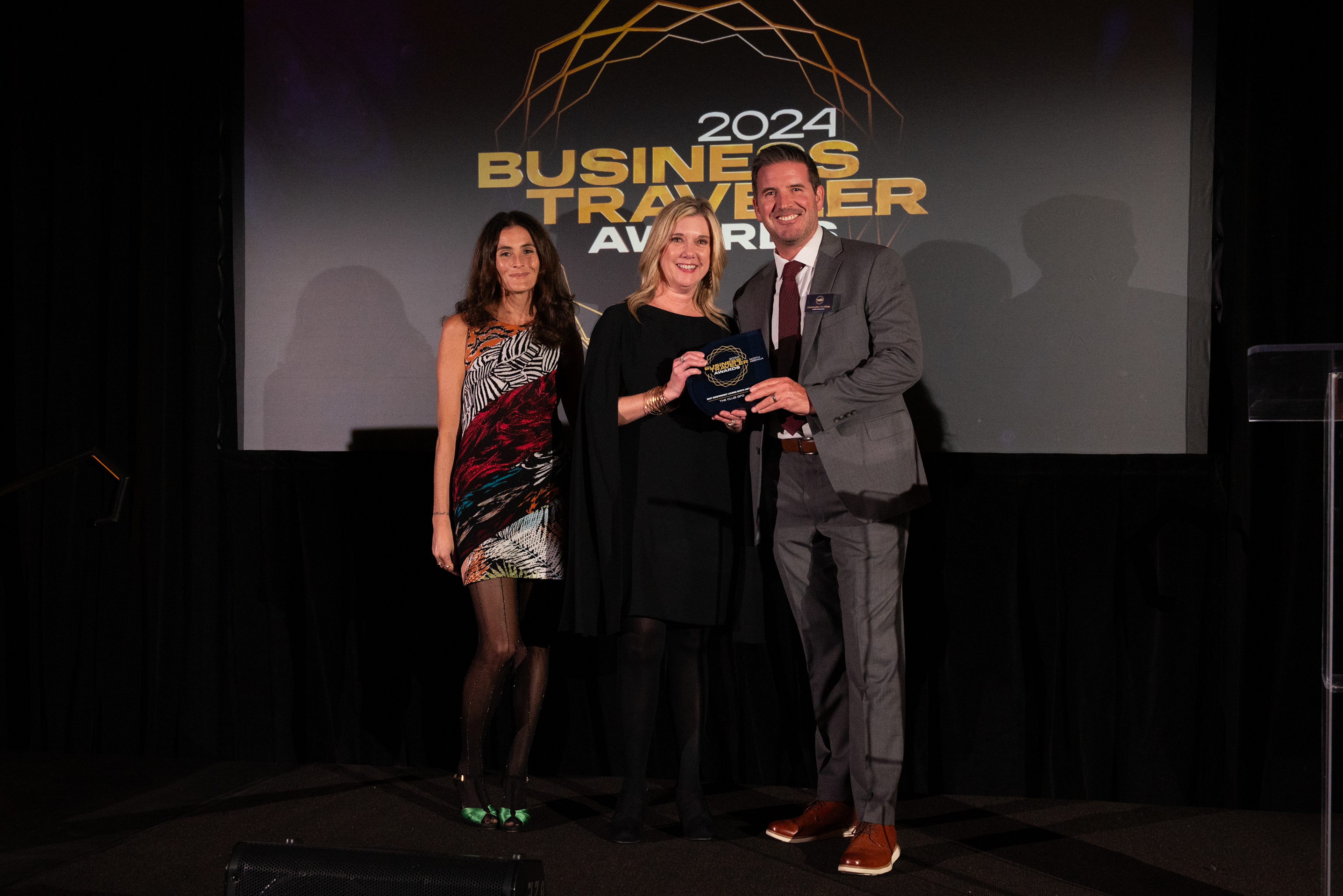 Two women and a man standing on stage holding an award at the Business Traveler Awards 2024. 