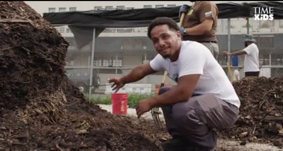 Domingo Morales pointing to a mound of composting material