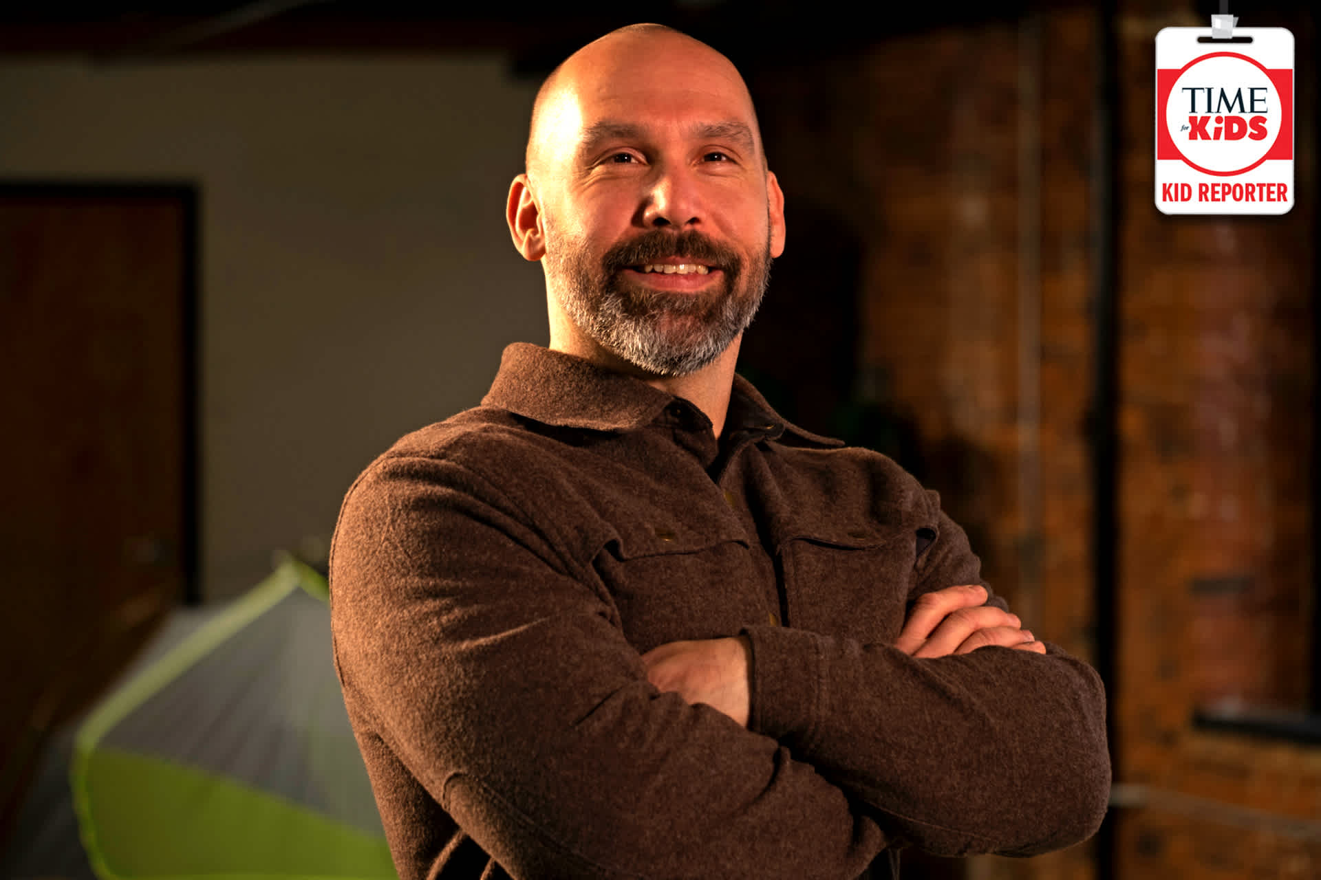 A smiling man standing in a room with a tent in the background