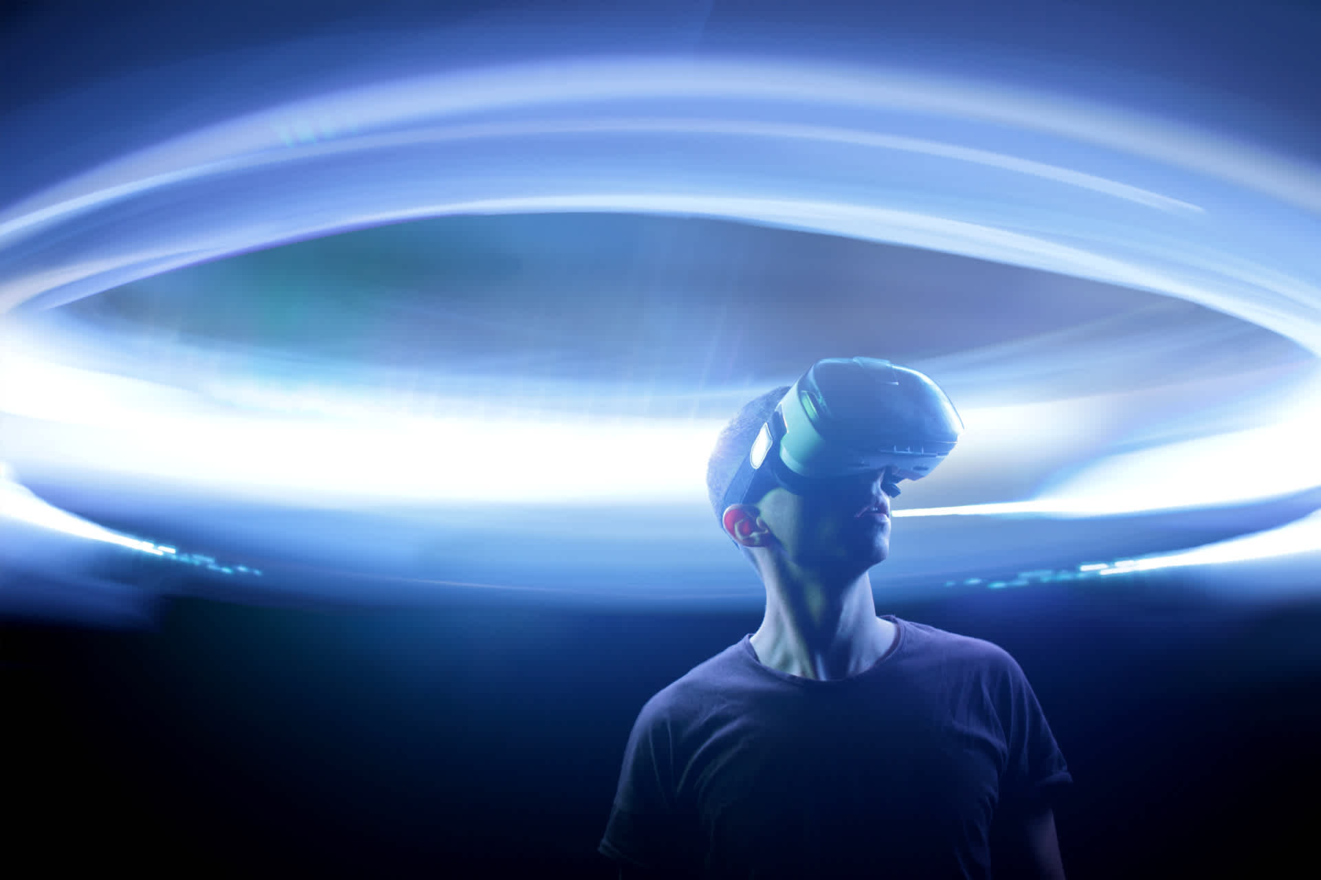 A teenager wearing a virtual reality headset stands in a dark room with a halo of light surrounding him