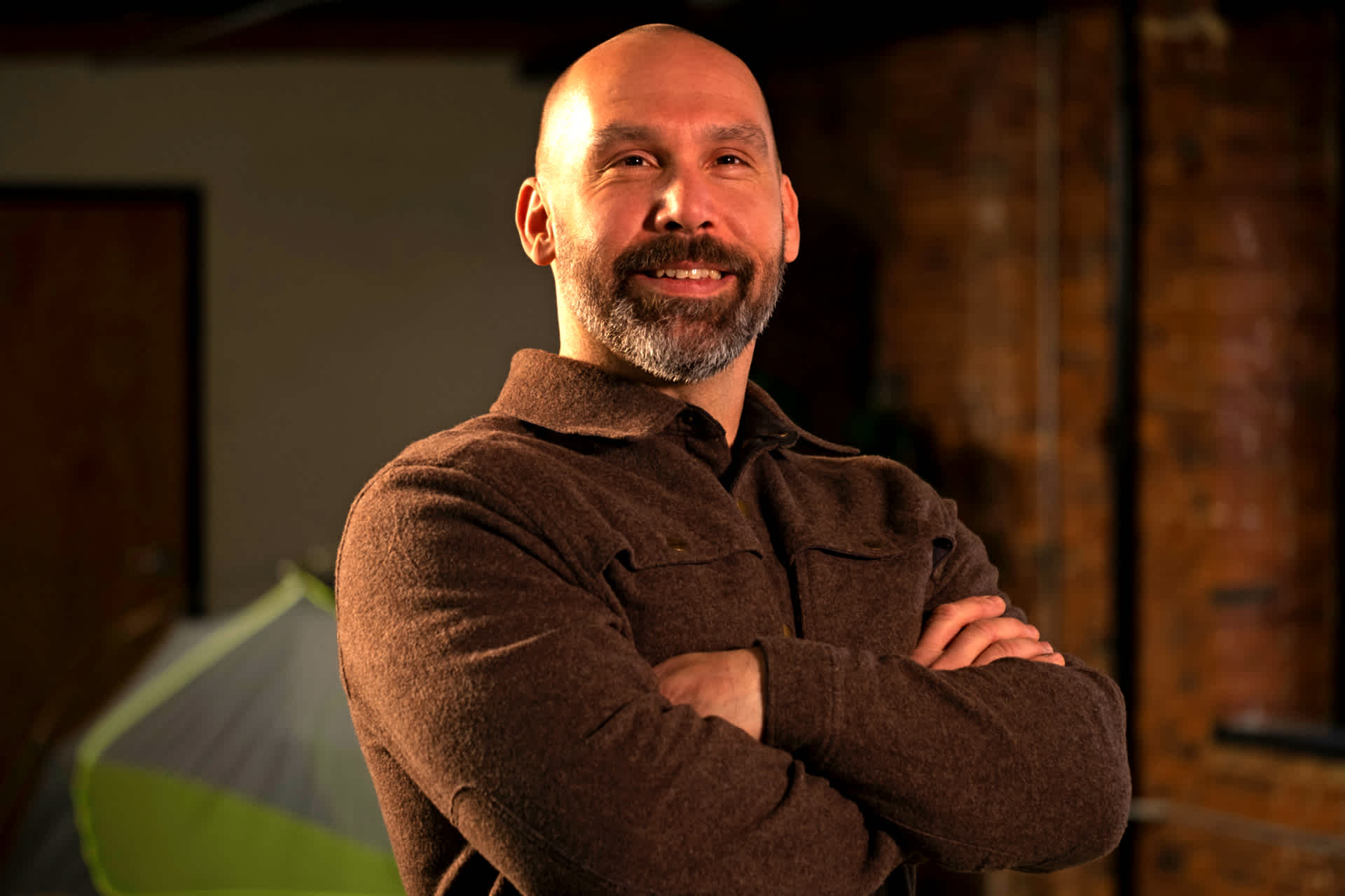 A smiling man standing in a room with a tent in the background