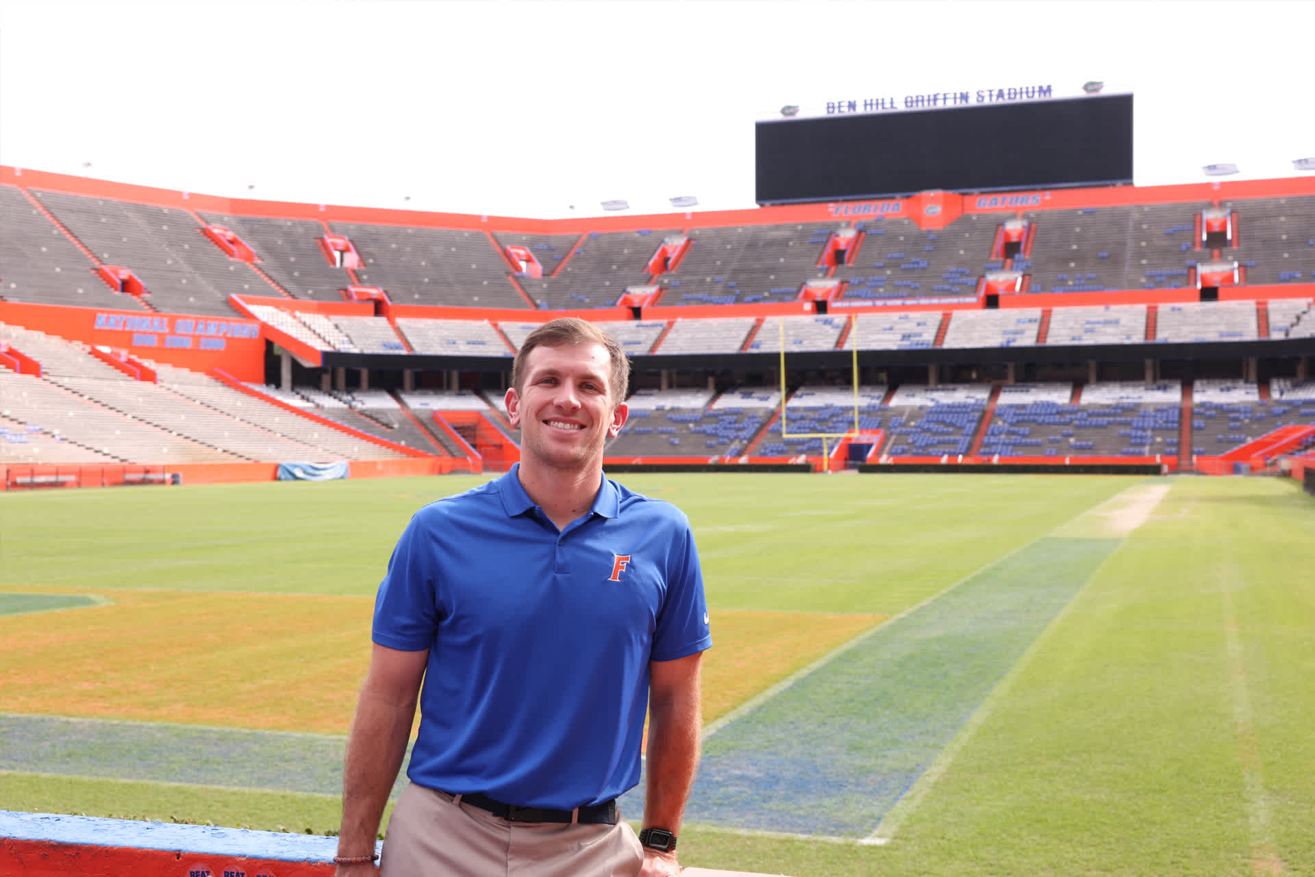 A man in a blue polo shirt with the Florida Gators football team logo poses in an empty stadium.