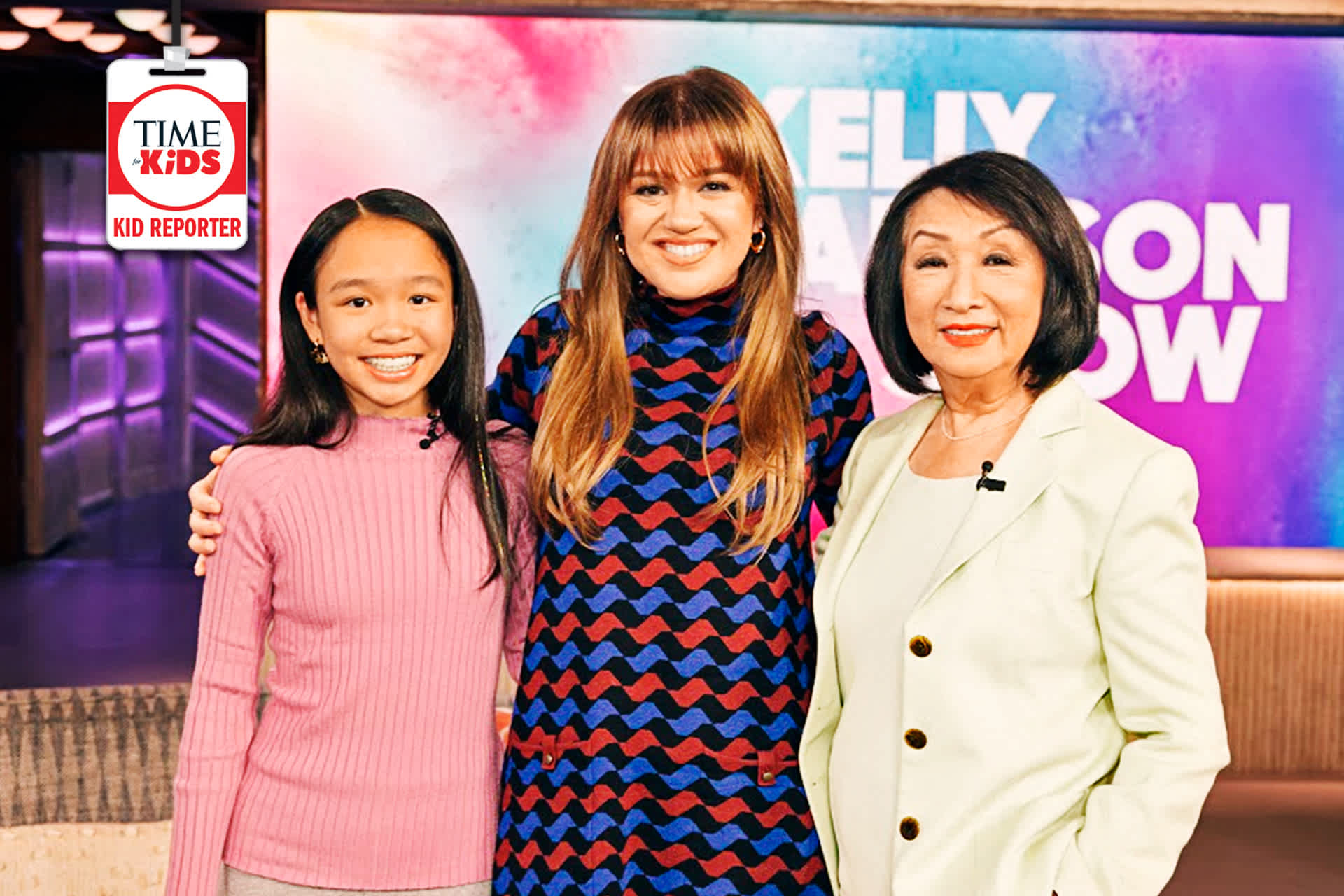 A girl stands with two women on the set of a talk show