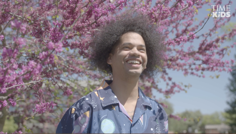 A man smiling in front of a pink flowering tree