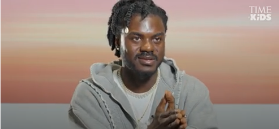 Artist Prince Gyasi holding his palms together against a pink and orange background