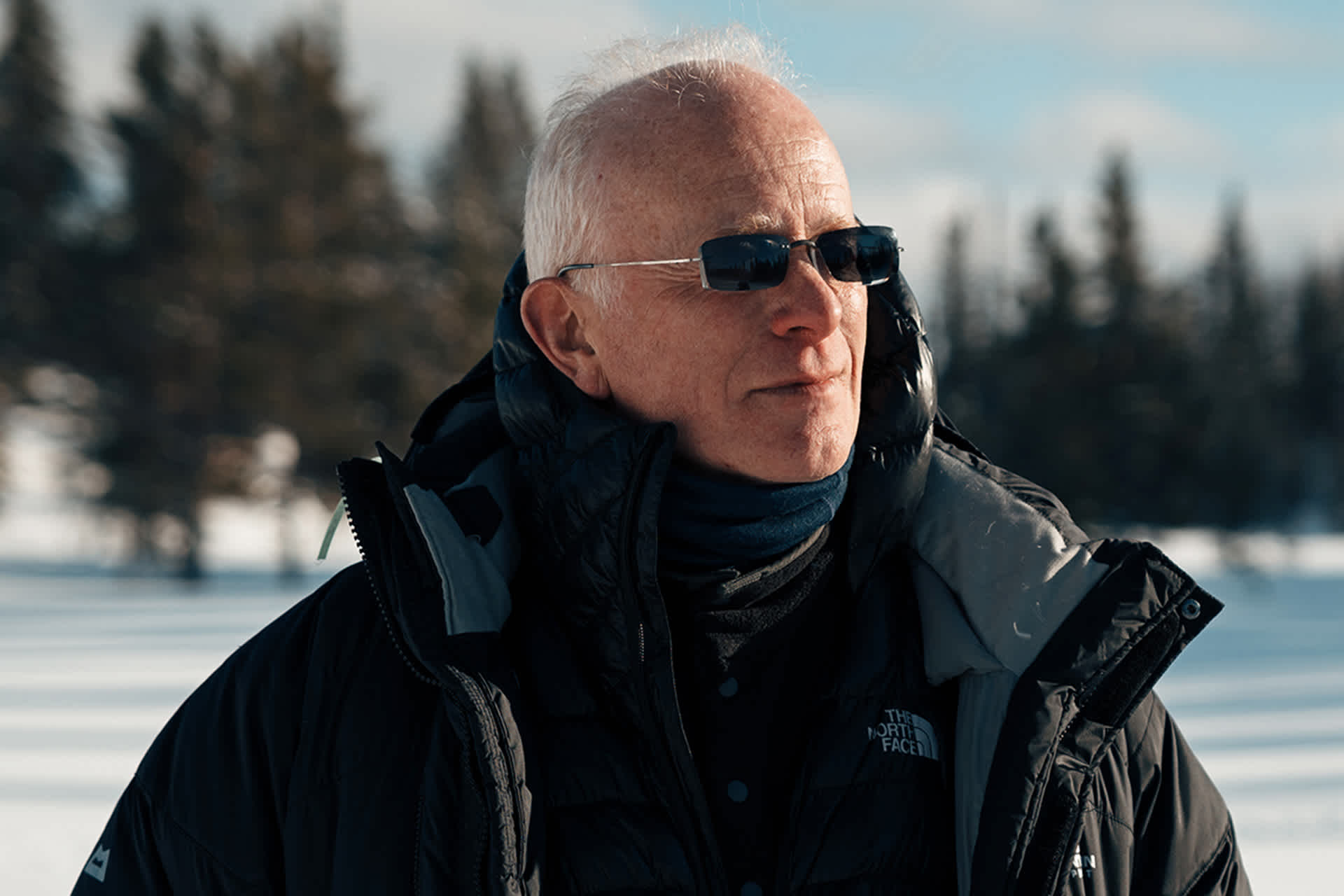 A man wearing sunglasses and a winter coat standing outdoors.