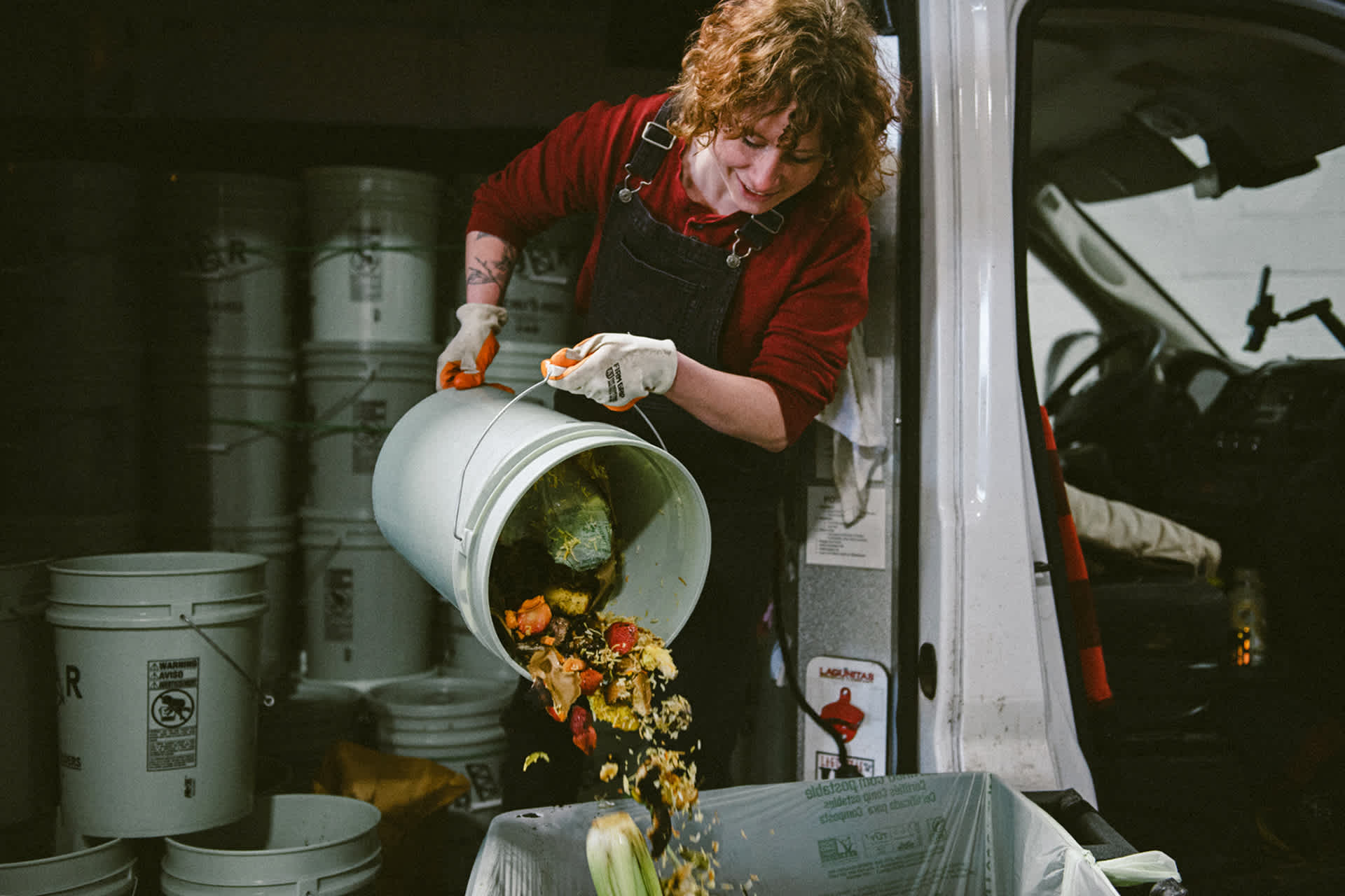 A worker pours a bucket of food scraps into a collection bin