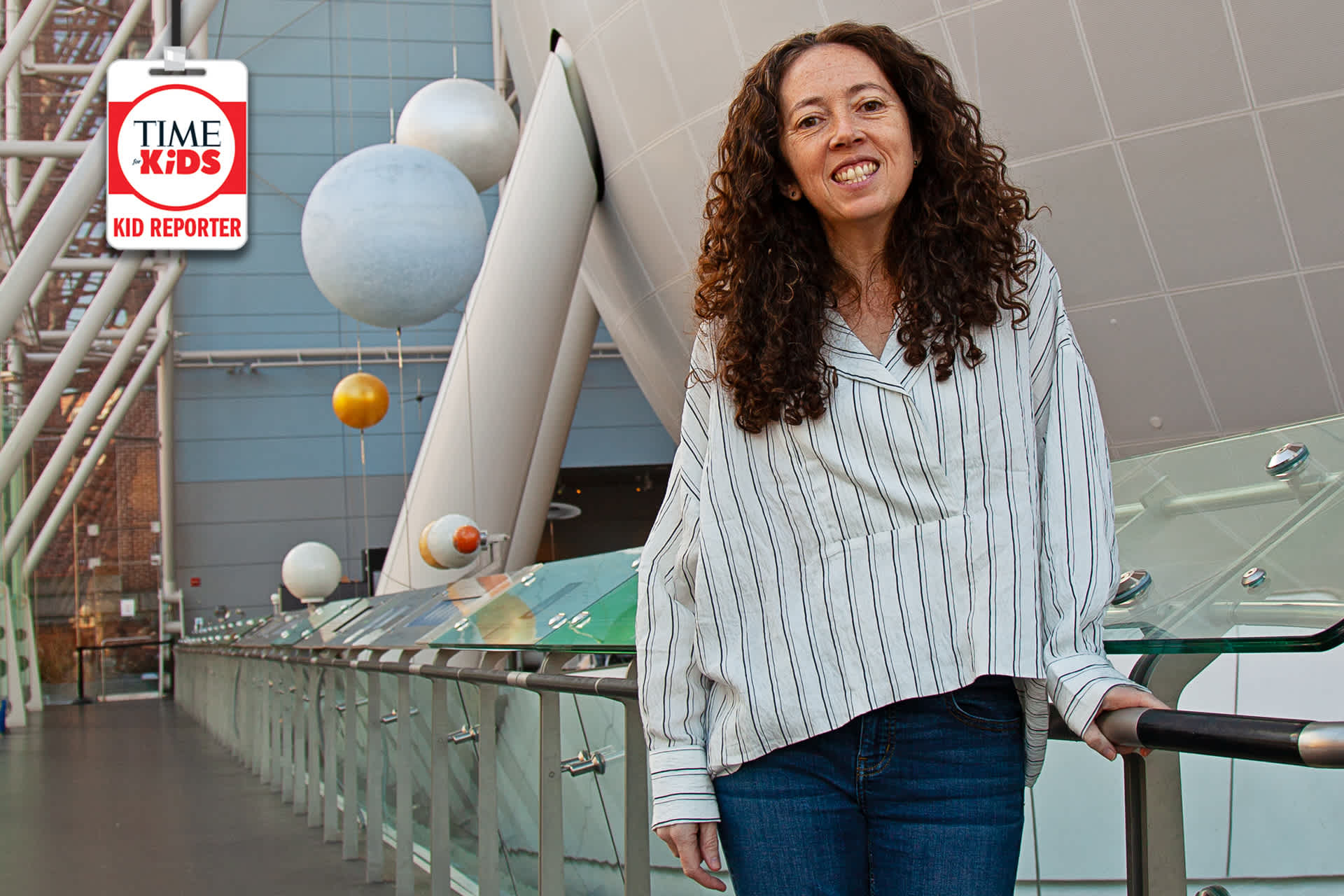 A woman standing in an atrium, with floating spheres behind her