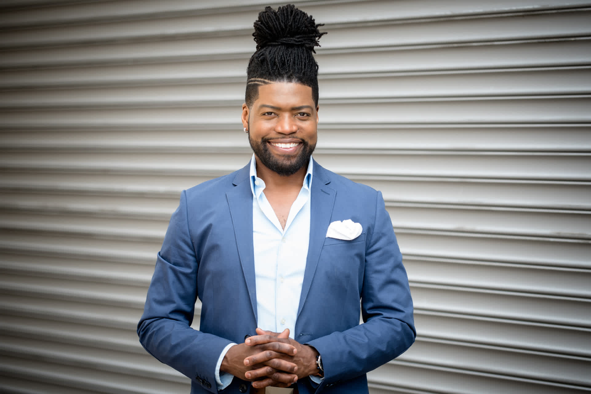 A man in a blue suit smiles as he poses against a gray background.