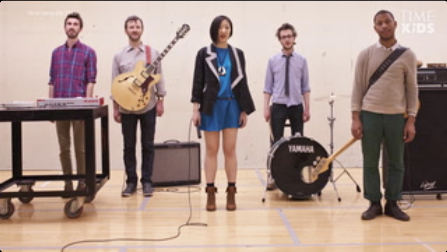 Young Jean Lee holding a microphone standing dead center flanked by two band members on her left side and two band members on her right side as they pose with instruments.