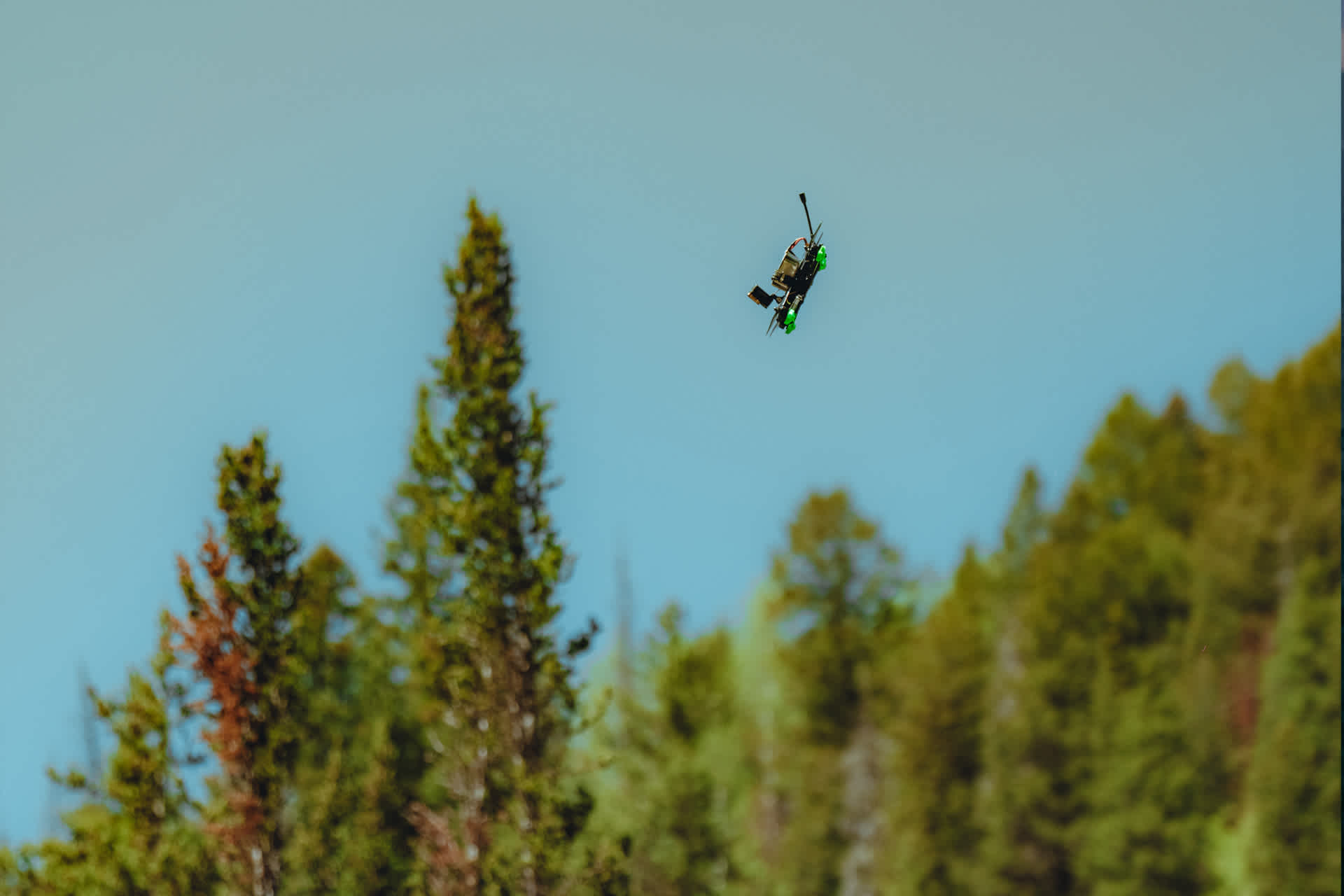 Drone flying through sky against backdrop of treetops.