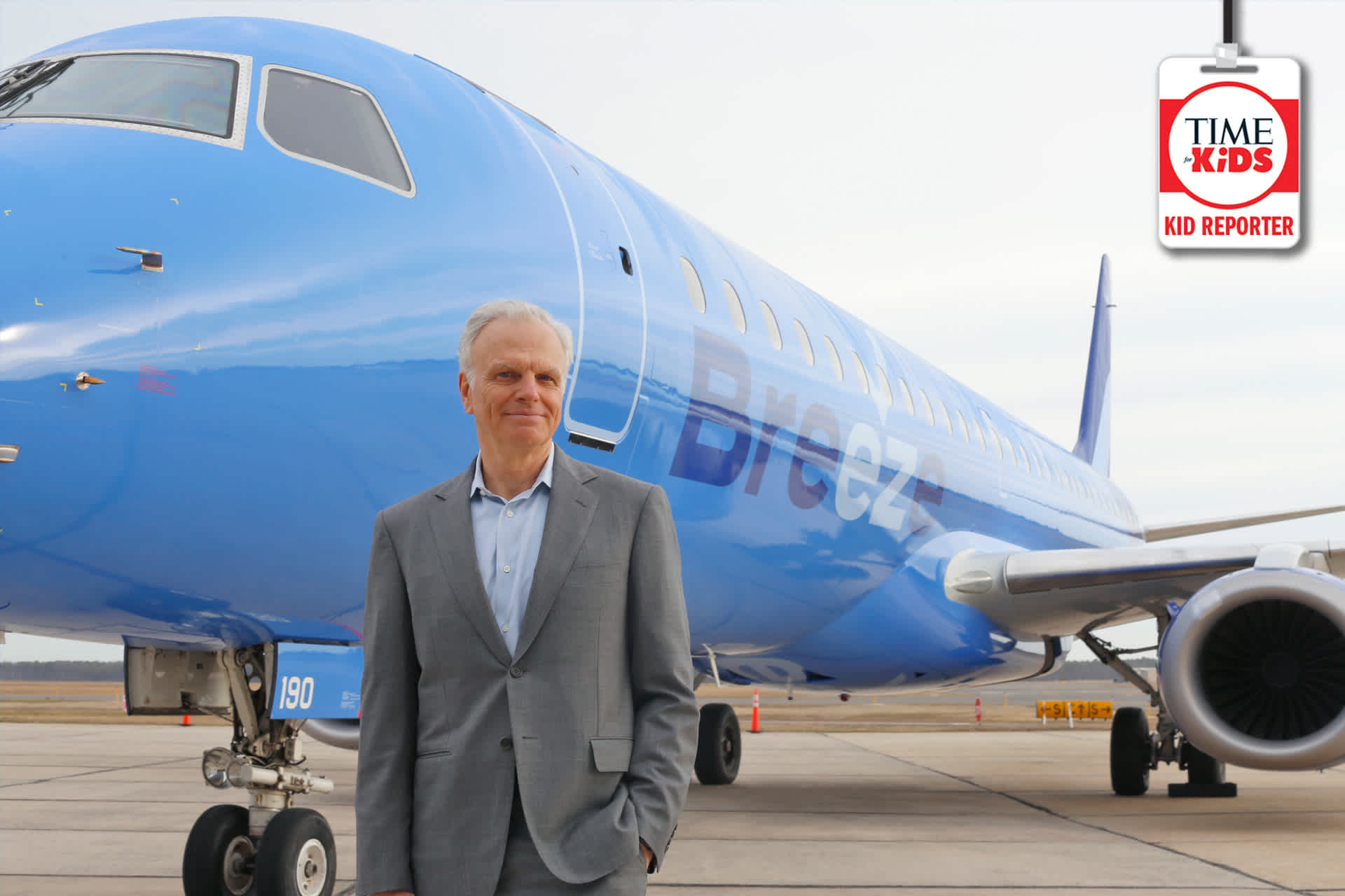 A man in a grey suit in front of a blue passenger jet with the word “Breeze” on its side.