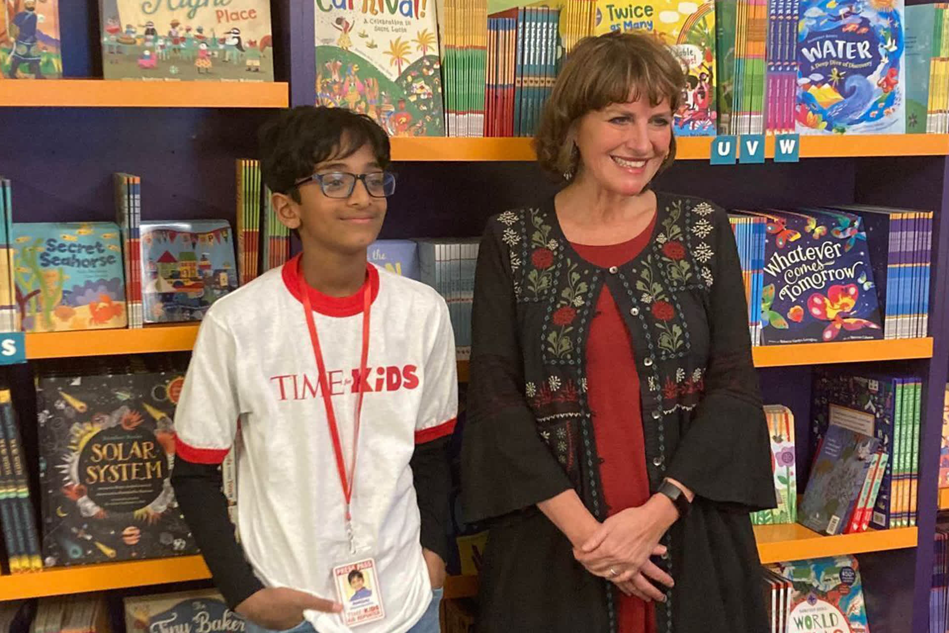 A boy and woman standing in front of bookshelves, smiling