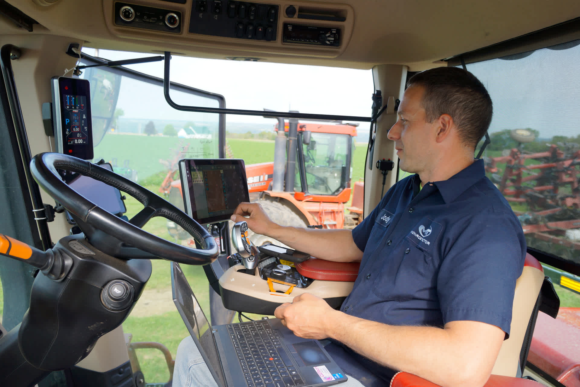 A man sits in the cab of a truck using a laptop and other modern technology.