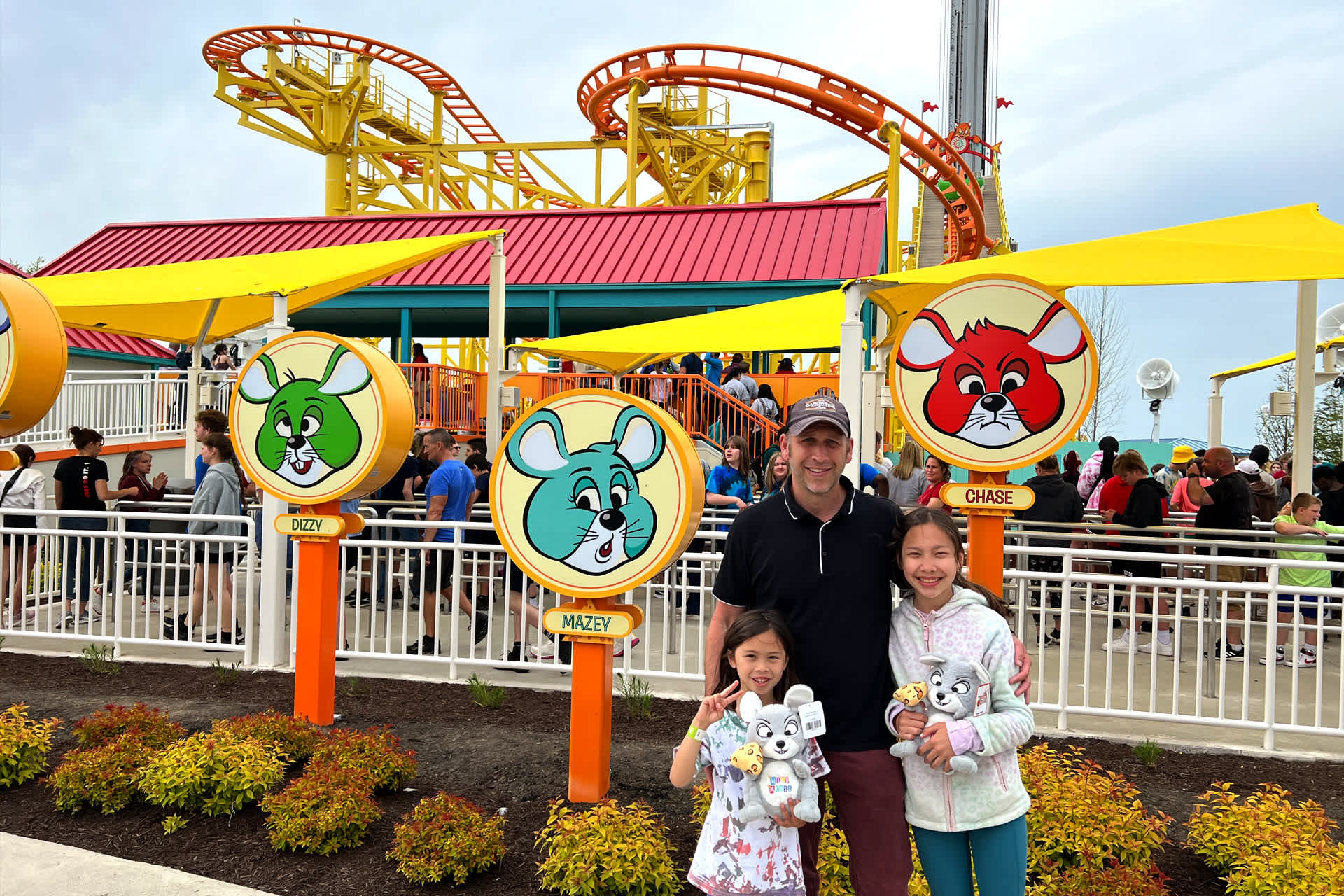 man with girls in front of roller coaster